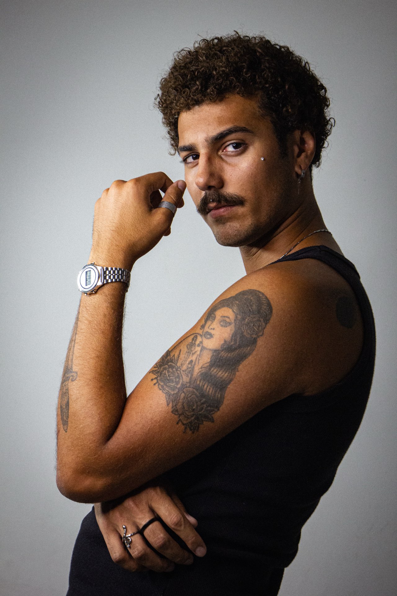 Danilo Lins de perfil, mão junto ao rosto e tatuagem no braço